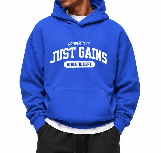 A man modeling a royal blue pullover hoodie with 'PROPERTY OF JUST GAINS' in white text, paired with black sweatpants and white sneakers, against a plain white background.